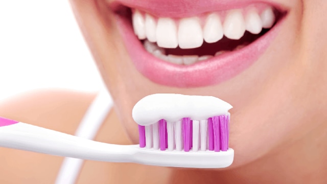Mujer sonriendo con dientes blancos y un cepillo de dientes blanco y rosa con pasta dental.