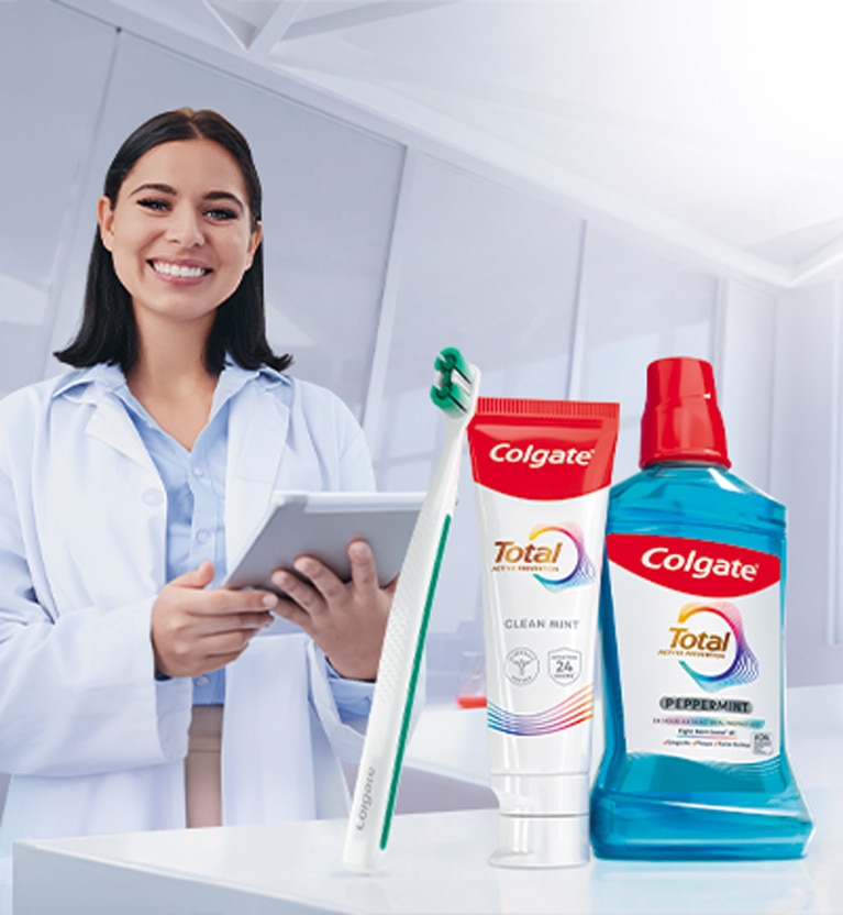 Dentista con tablet junto a crema dental, cepillo y enjuague Colgate Total para el Mes de la Salud Oral.