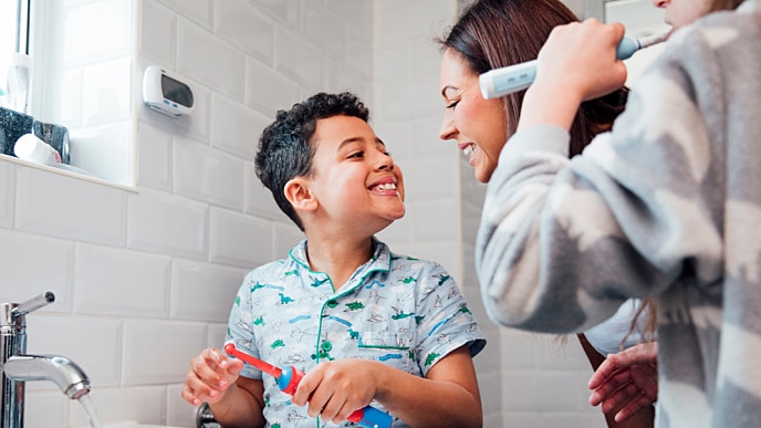 Madre e hijo sonriendo mientras lavan sus dientes con cepillo eléctrico